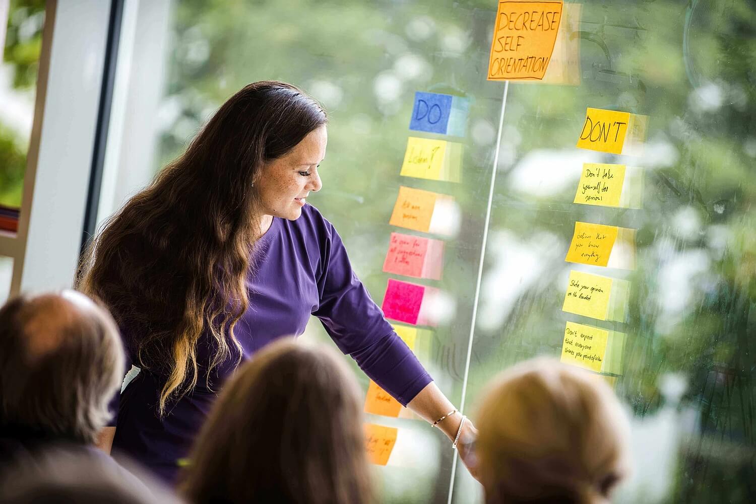 Evelien Rose eine Scrum.org Trainerin steht vor einer Fensterscheibe (beklebt mit Notizzetteln) und erläutert Scrum Prinzipien
