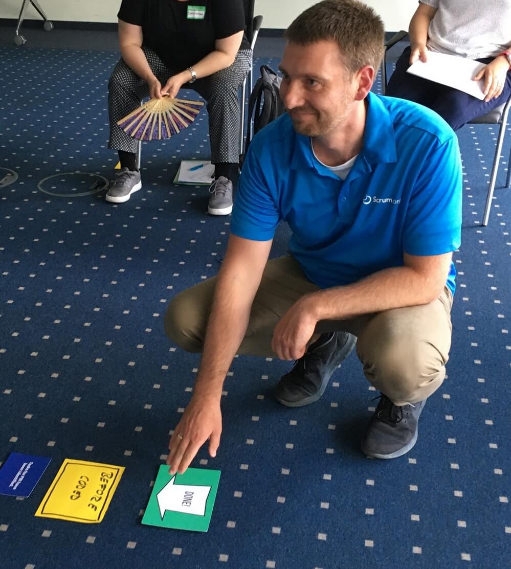 eine Person kniet vor ein paar Karten die auf den Boden liegen und für eine Übung im Scrum Master II Training verwendet werden